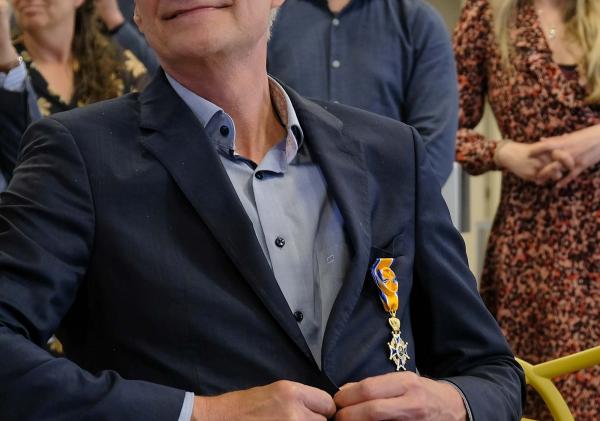 Man die zijn jasje dichtdoet en een oranje lintje heeft opgespeld