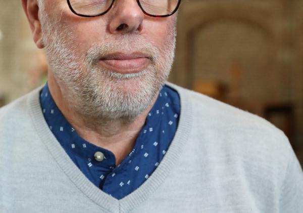 Man met een bril, grijze trui en een oranje lintje