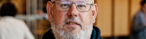 Man met grijze baard, bril en blauwe trui met capuchon