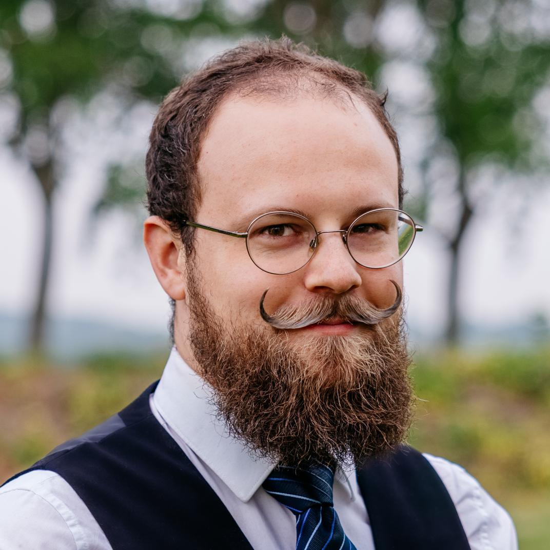Man met ronde bril, krulsnor, baard, overhemd en streepjesstropdas